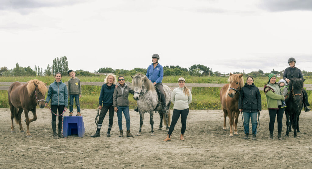 Photo de groupe de l’association Libea : plusieurs membres de l’équipe, adultes et enfants, posent en extérieur avec des chevaux islandais, certains montés, d’autres tenus en main, devant une clôture en bois et un paysage verdoyant.