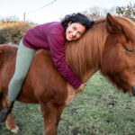 Rhyanna, jument islandaise alezane, avec Tabea de l’association Libea allongée sur son dos dans un pré breton, moment de complicité et de calme