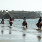 Quatre cavalières de l’association Libea partent en balade sur leurs chevaux islandais, entrant dans la mer au pied des falaises bretonnes, lors de la prestation Mer & Bruyère.